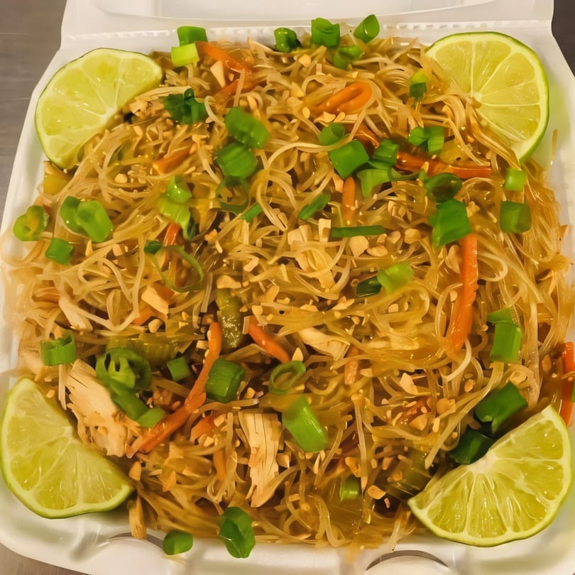 Filipino pancit bihon noodles with chicken, vegetables, peanuts, green onions, and lime wedges.